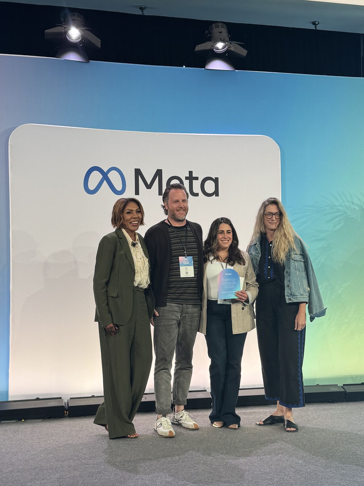 Four people standing on stage at a Meta event, smiling and posing with an award in front of a Meta-branded backdrop, representing dentsu X.
